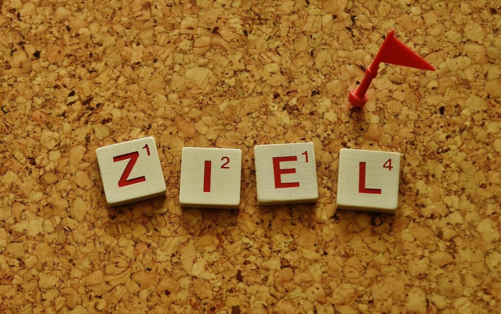 Scrabble-Steine mit dem Wort „ZIEL“ und einer roten Fahne auf einer Korktafel – Symbol für Zielarbeit, SMART-Ziele und Mentaltraining zur Zielerreichung